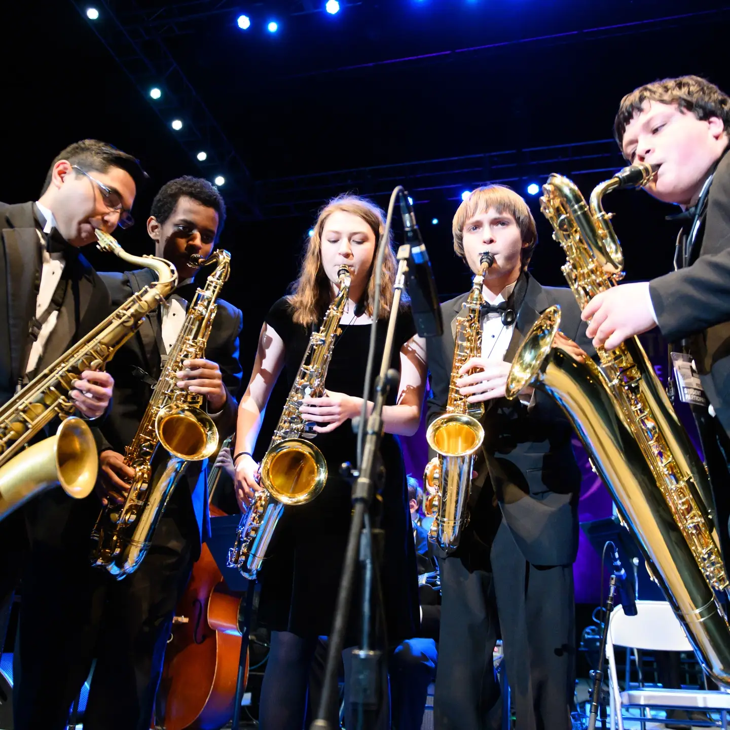 Student saxophonists gather around a microphone while playing at an LHJF concert.
