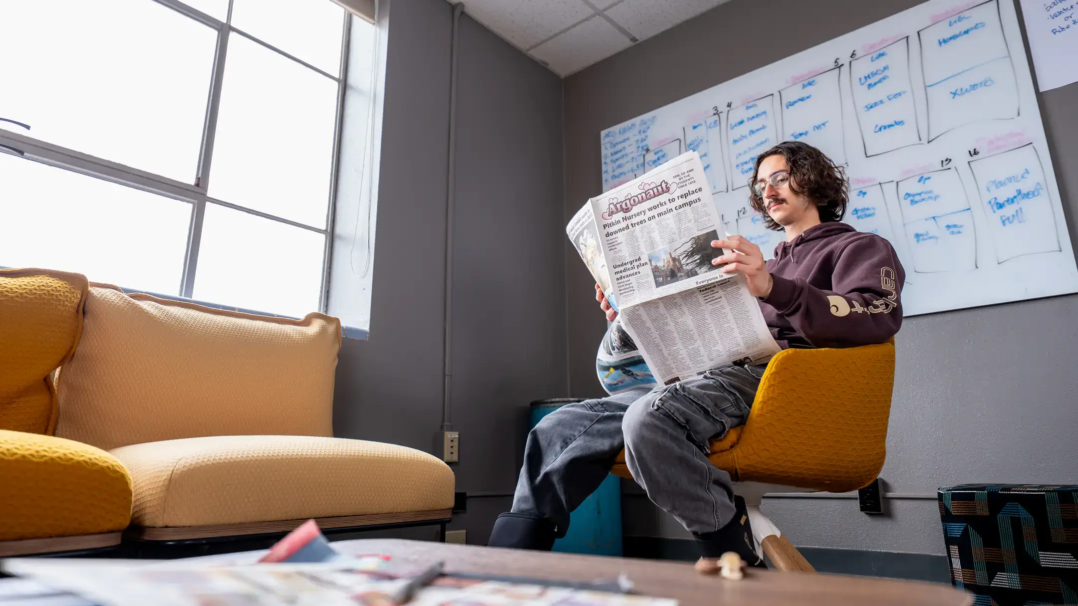 A student reading a newspaper in a yellow lounge chair