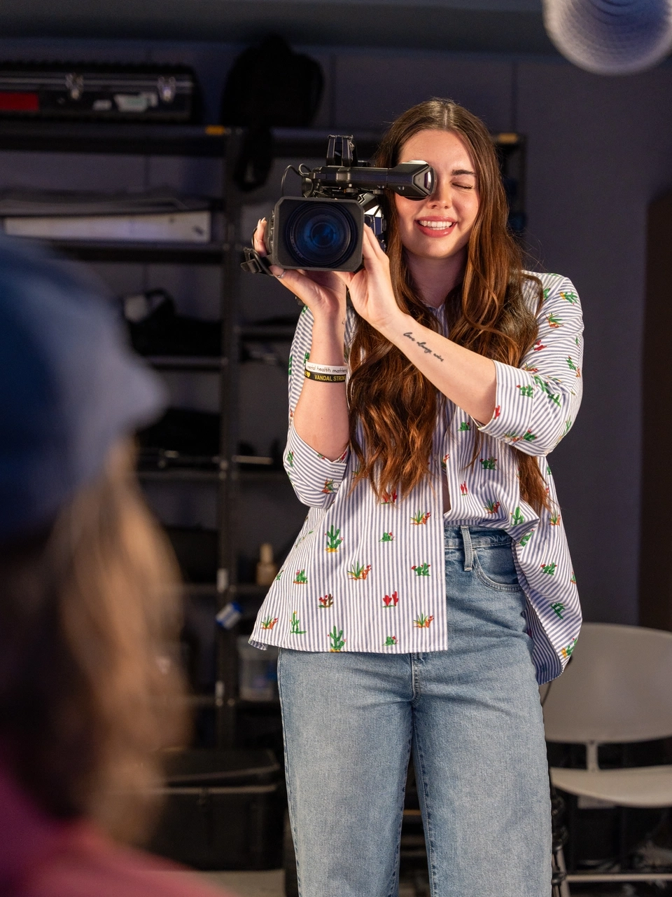 Woman stands in film studio looking through a film camera.
