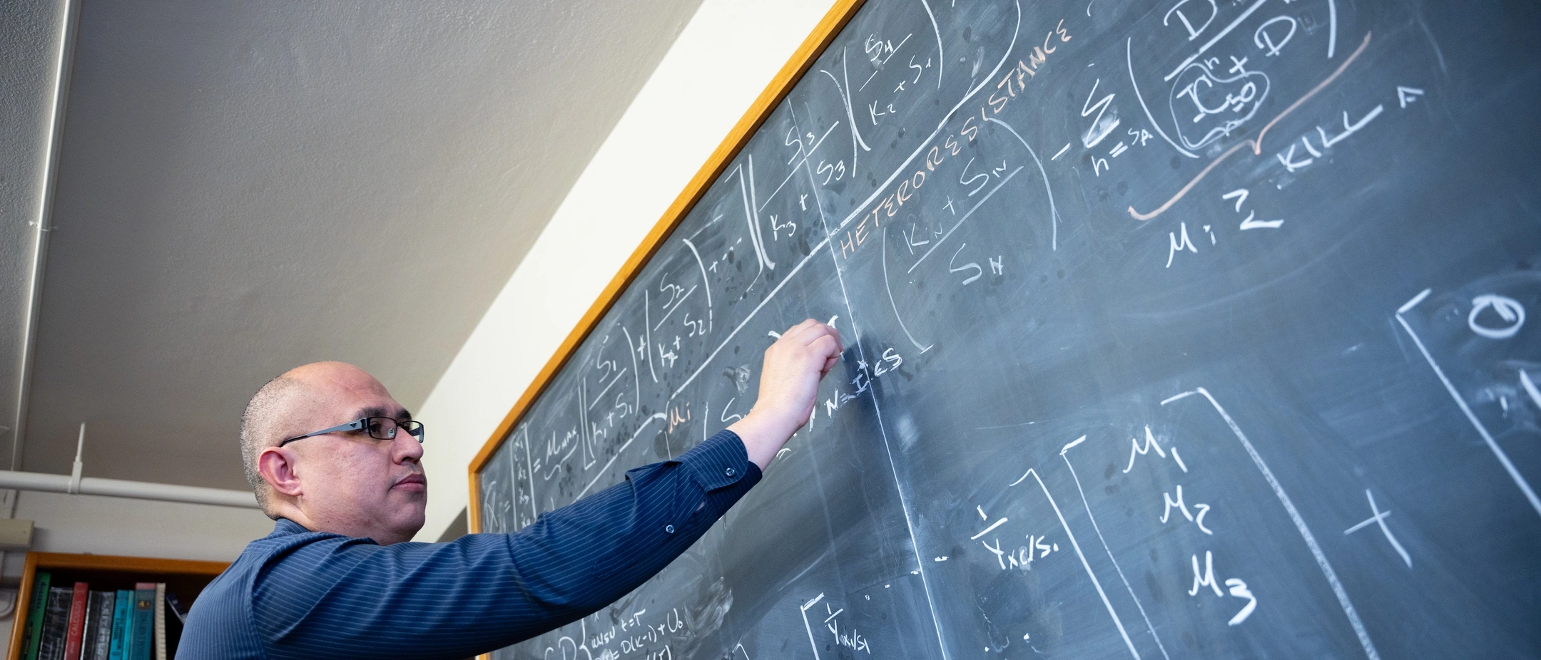 Assistant Professor of Mathematics, Esteban Hernandez-Vargasriting, presenting math equations model on a chalkboard to study the mitigation of viral infections.