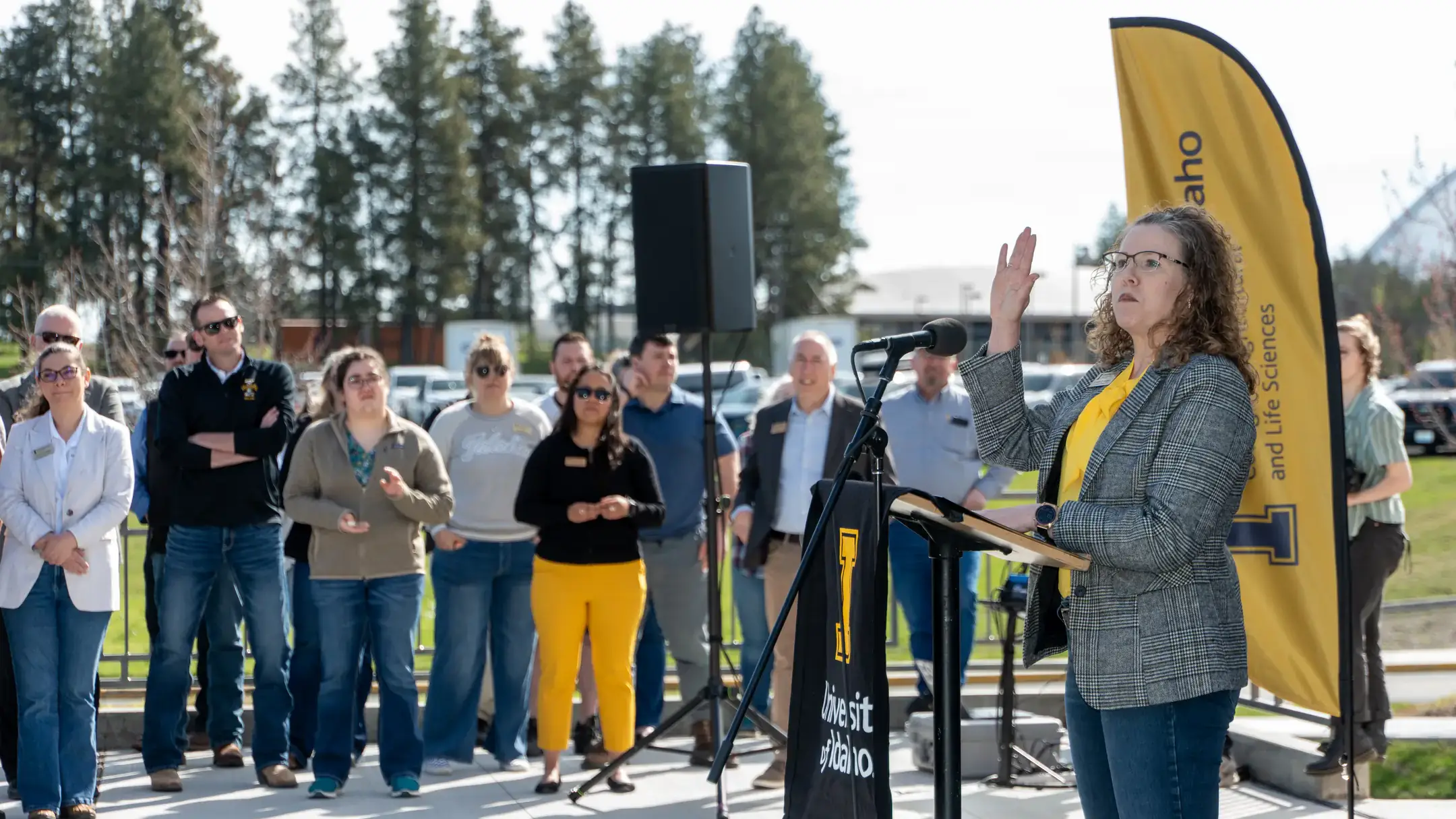 A dean holds up her hand as she addresses a large crowd.