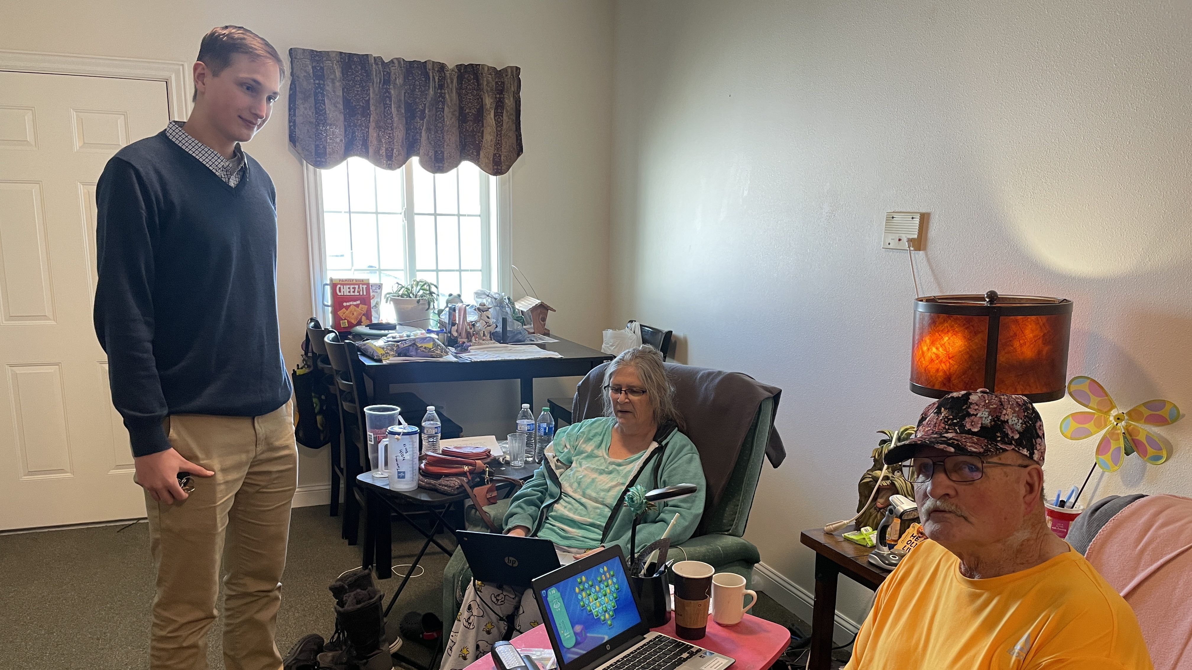 A man helping an elderly couple with their laptops in their home.