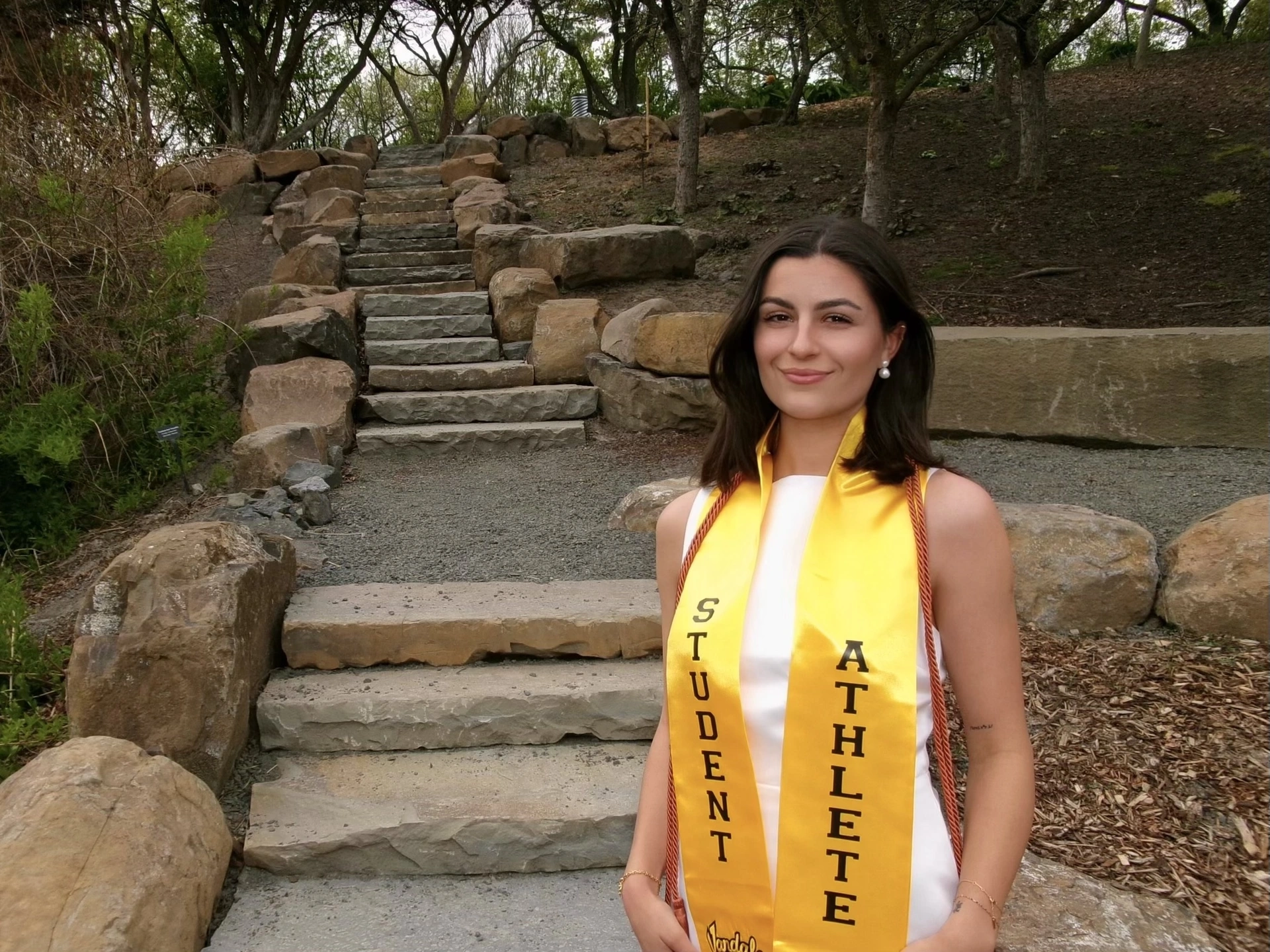 Saffron Dowse standing with student athlete regalia, outside near stone landscaping.