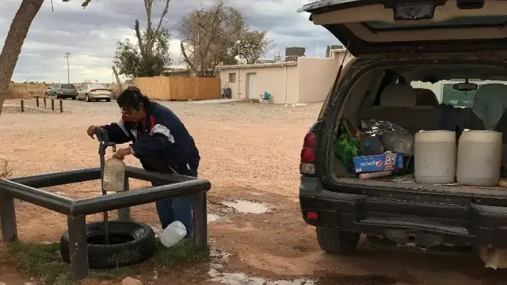 A woman fills a jug from an outdoor spicket.