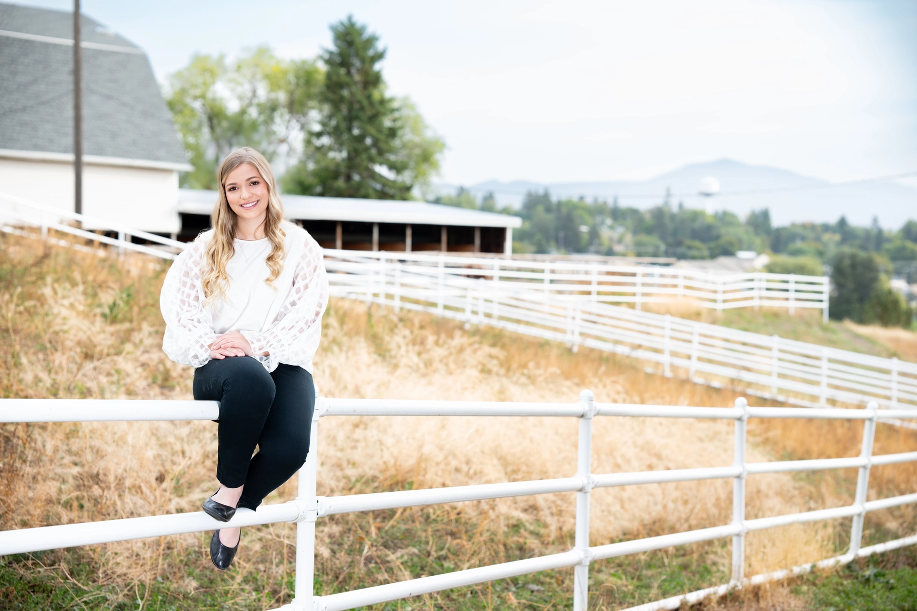 A woman sitting on a white fence.