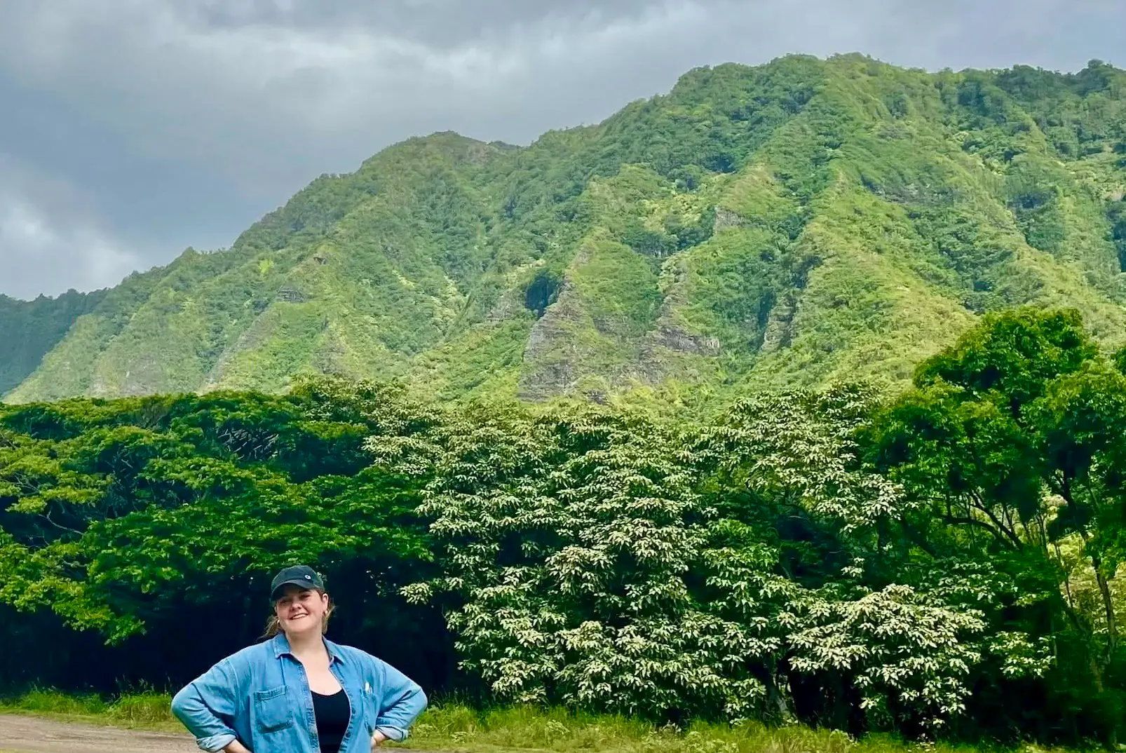 Elena Doss smiling at the base of a lush mountain range in Hawaii.