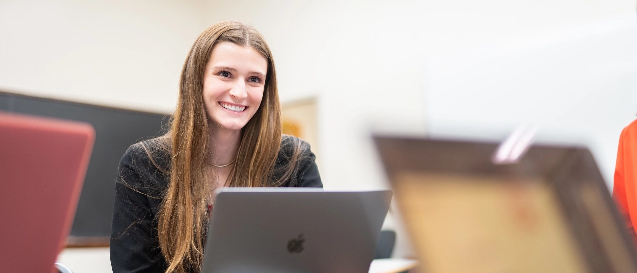 A smiling student sits at a desk with a laptop.