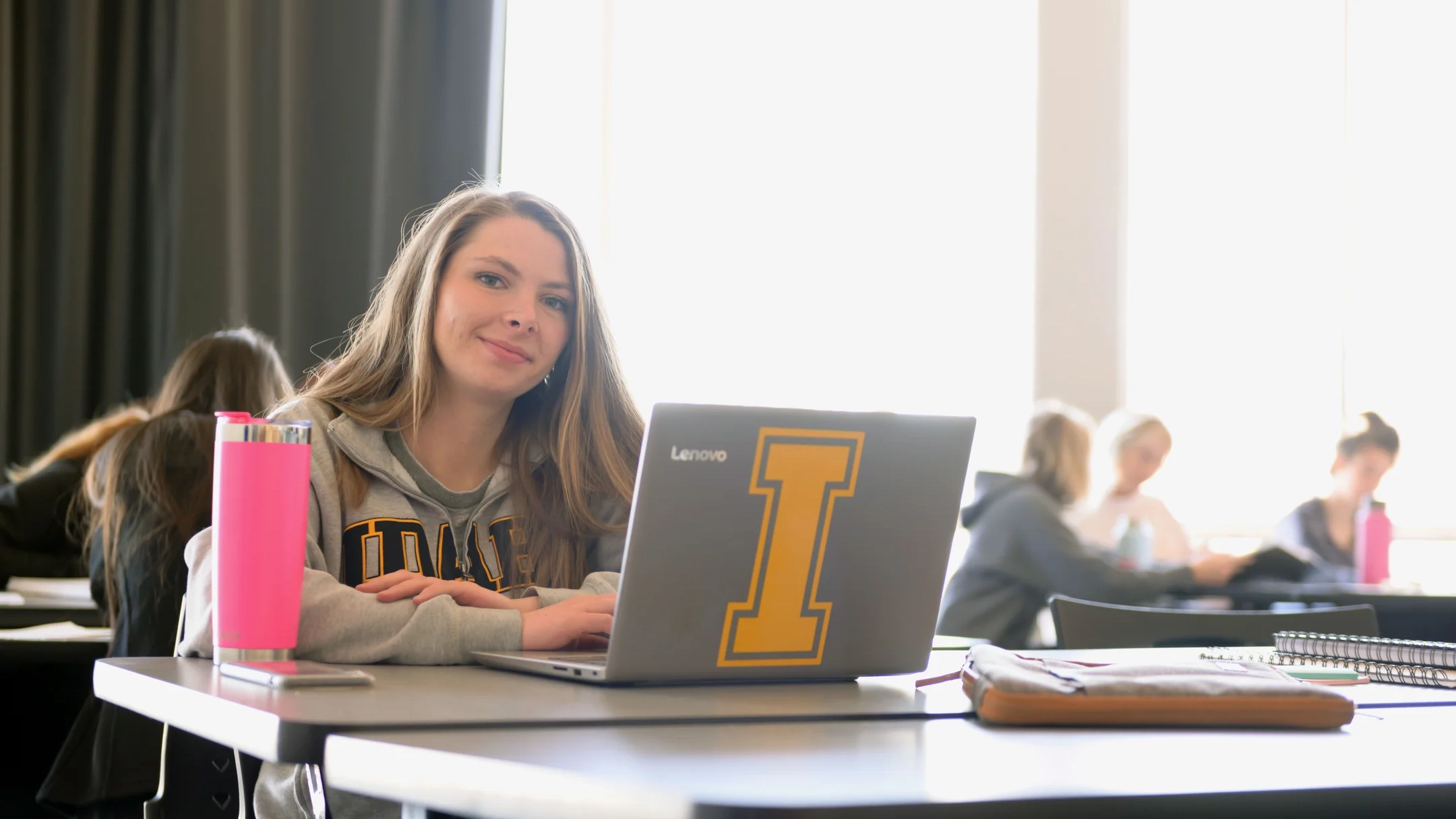 International student sitting at a table behind a laptop looking at the camera. 