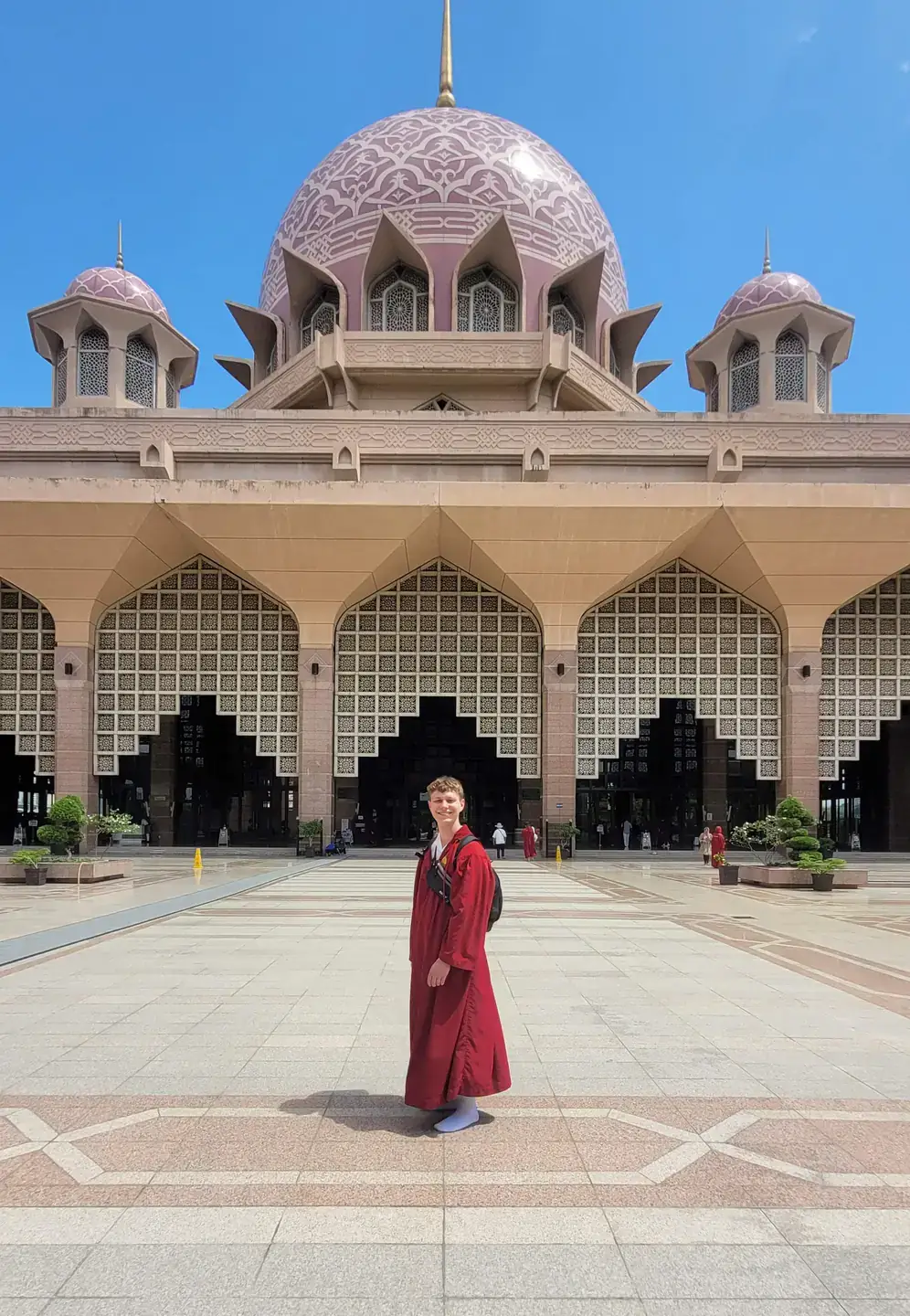 Man in a red robe standing in front of a large while marble building with a dome.