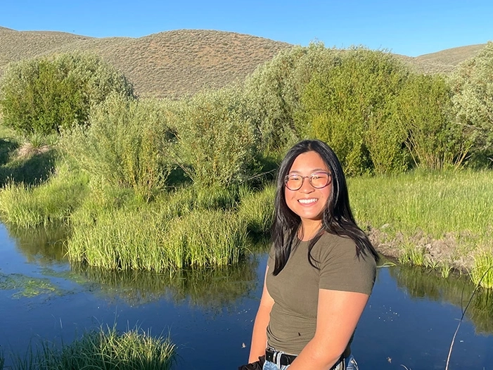 A woman stands in front of a rangeland pond.