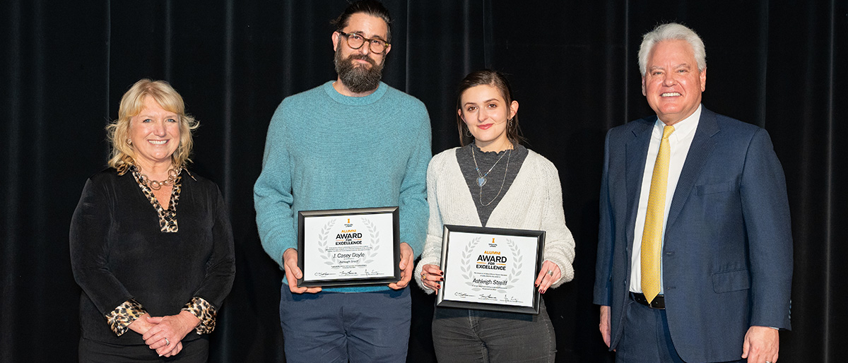 Four people posing for camera, with two holding certificates.