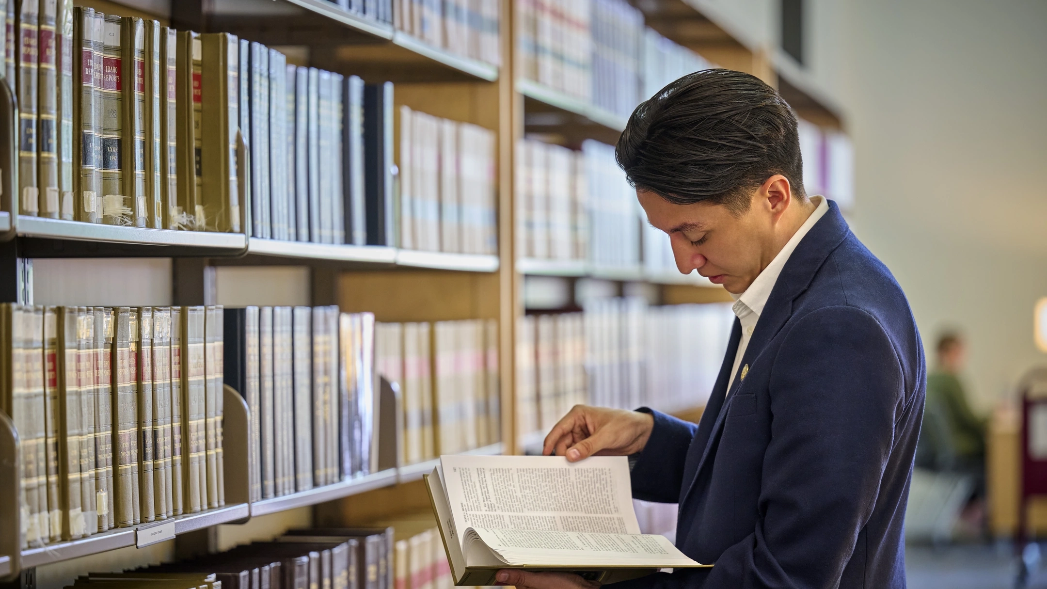 Student standing in front of library shelves reading a book.