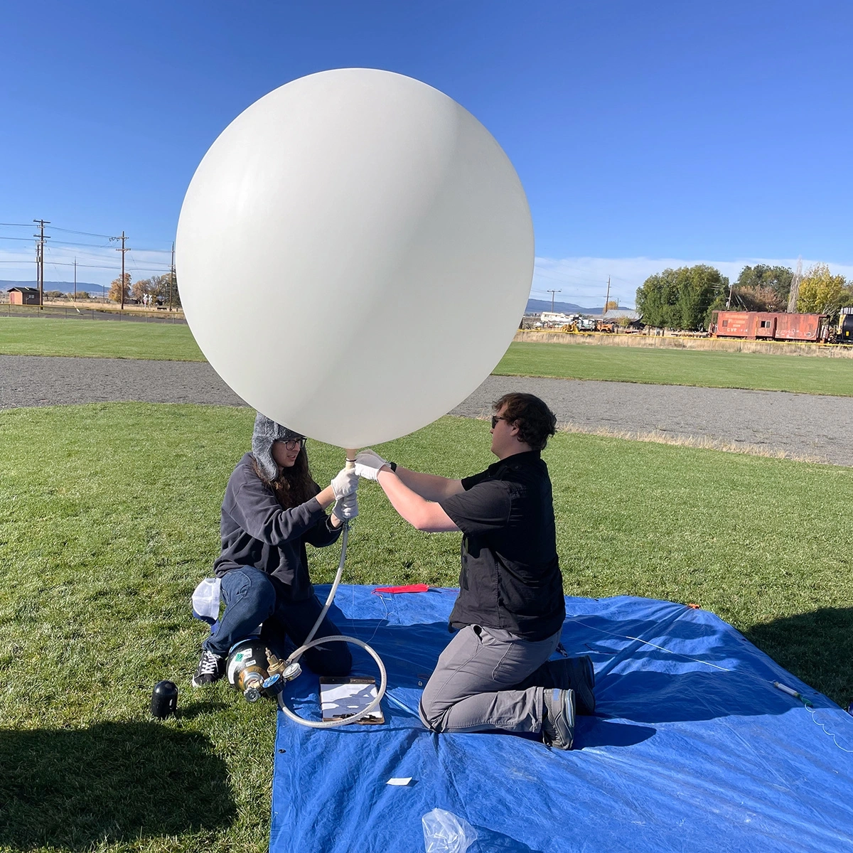 Two people fill a white weather balloon.