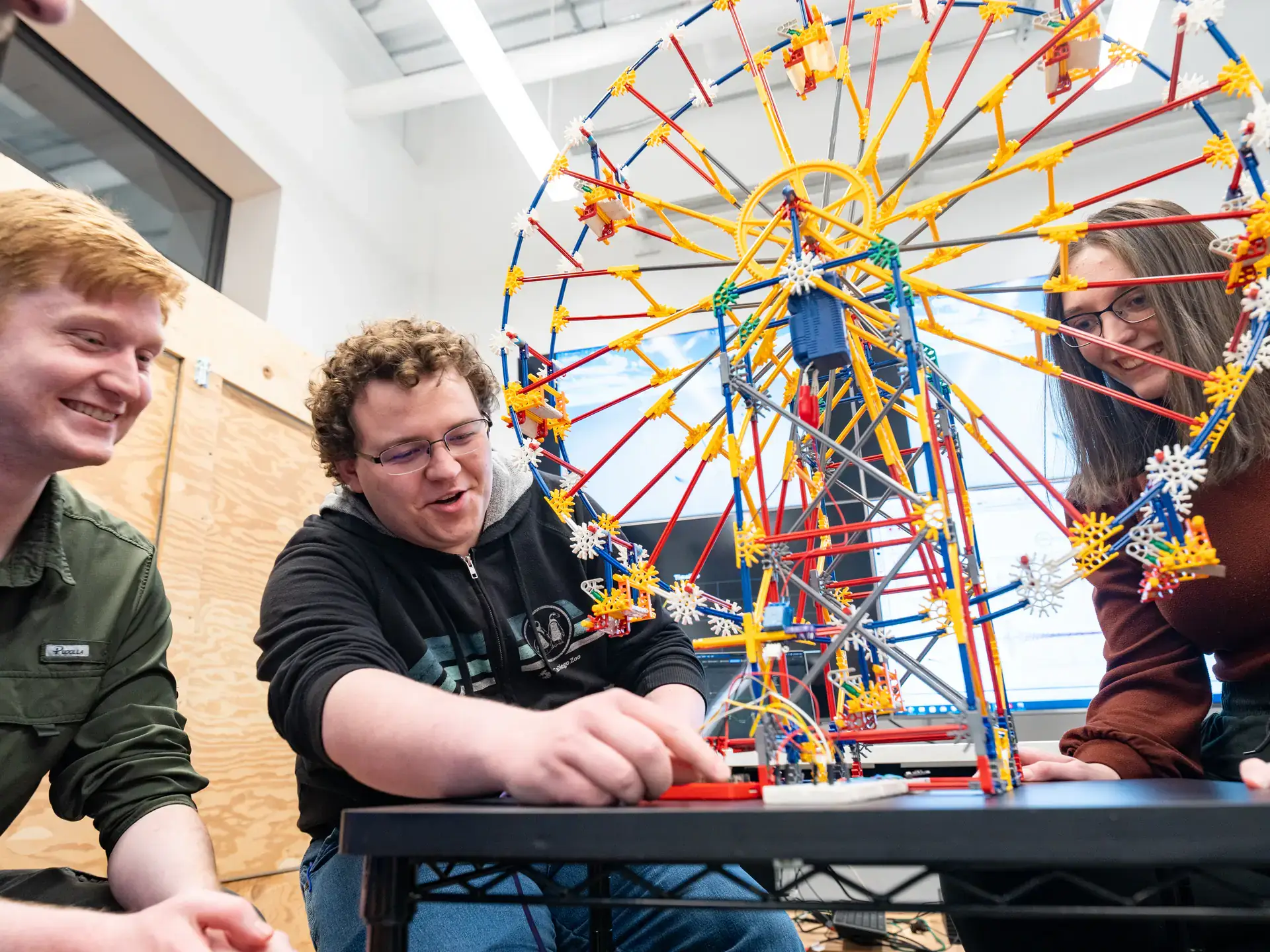 Photos of upcoming graduates in the cyber security program showing off a model ferris wheel which replicates how a cyber attack could affect mechanical processes.
