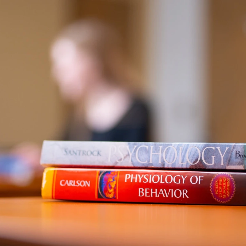 Two psychology books on a table with a student in the distant background