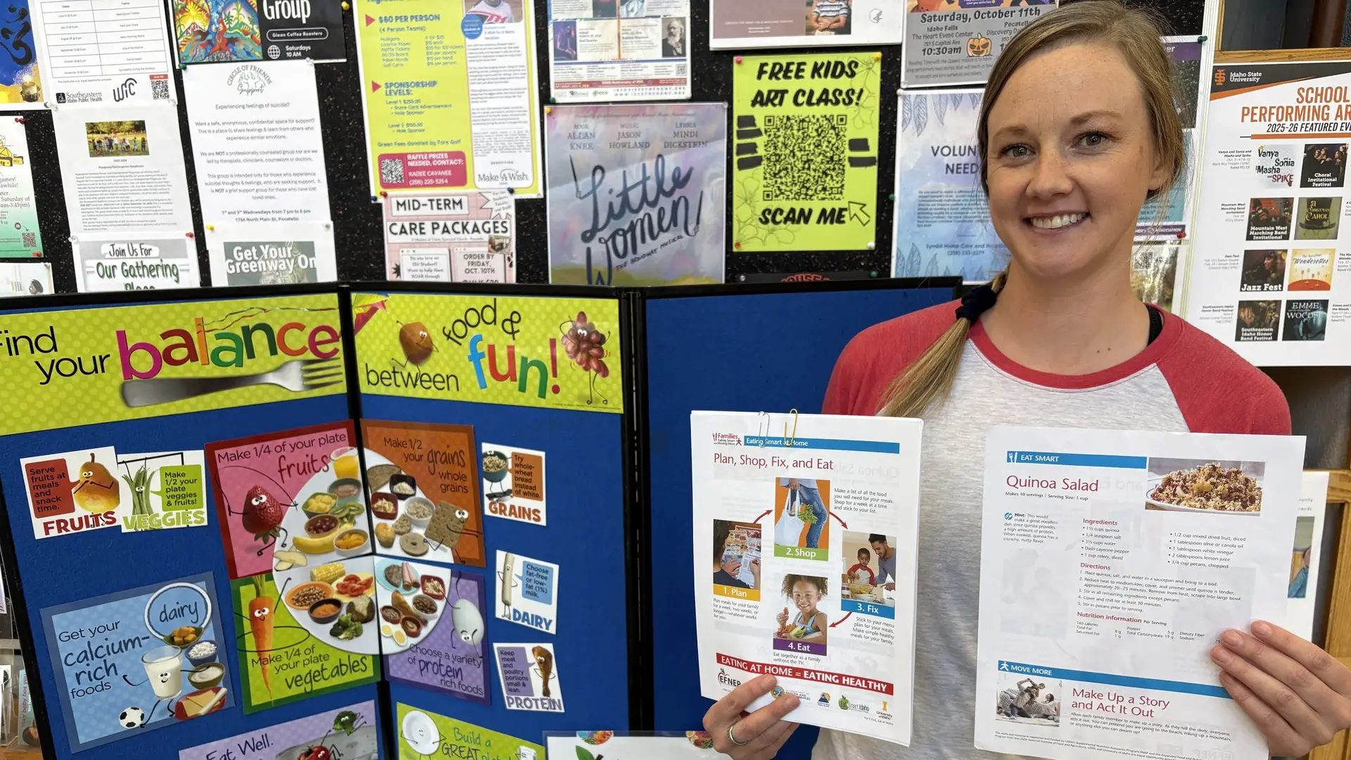 Eat Smart Idaho Nutrition Instructor Jessica Hansen holds program brochures about nutrition, standing by a blue poster featuring information about food groups.