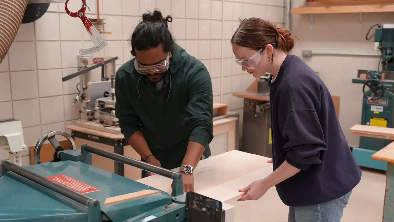 Two people push a piece of wood through a saw.