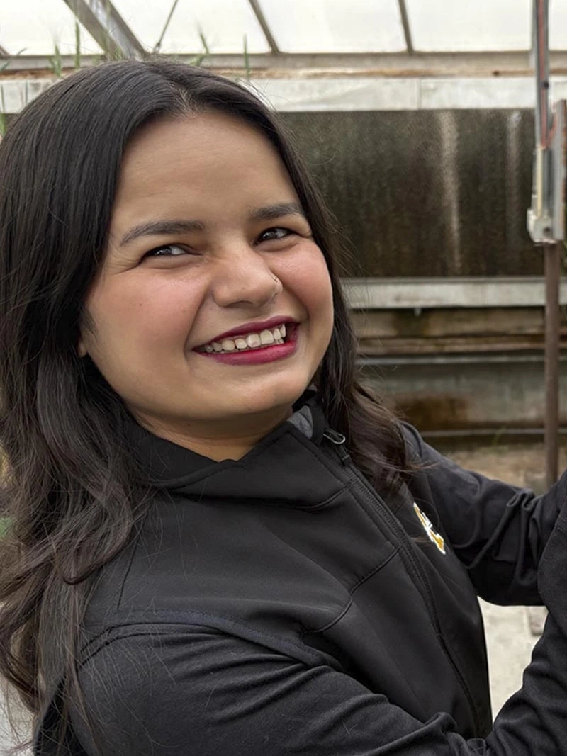 Pabitra Joshi smiles while wearing Vandal Gear in a greenhouse.