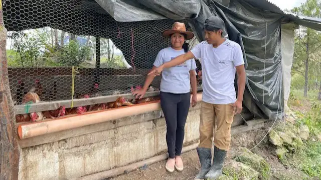 A Guatemalan boy and girl stand in front of a chicken coup.