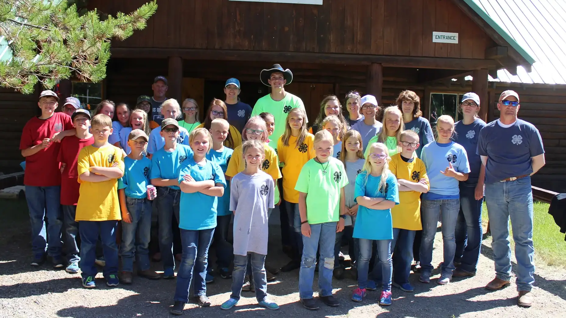 4-H youth pose outside cabin with 4-H clover logo