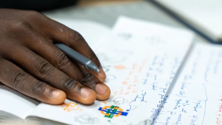 A hand presses on a page filled with color-coded notes and design sketch.