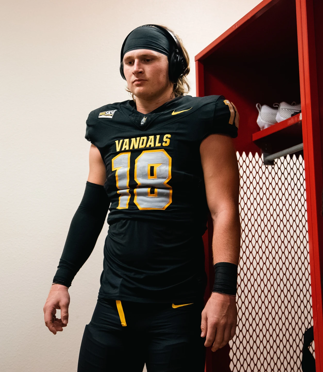 Tommy McCormick listens to headphones in his black uniform in the locker room.