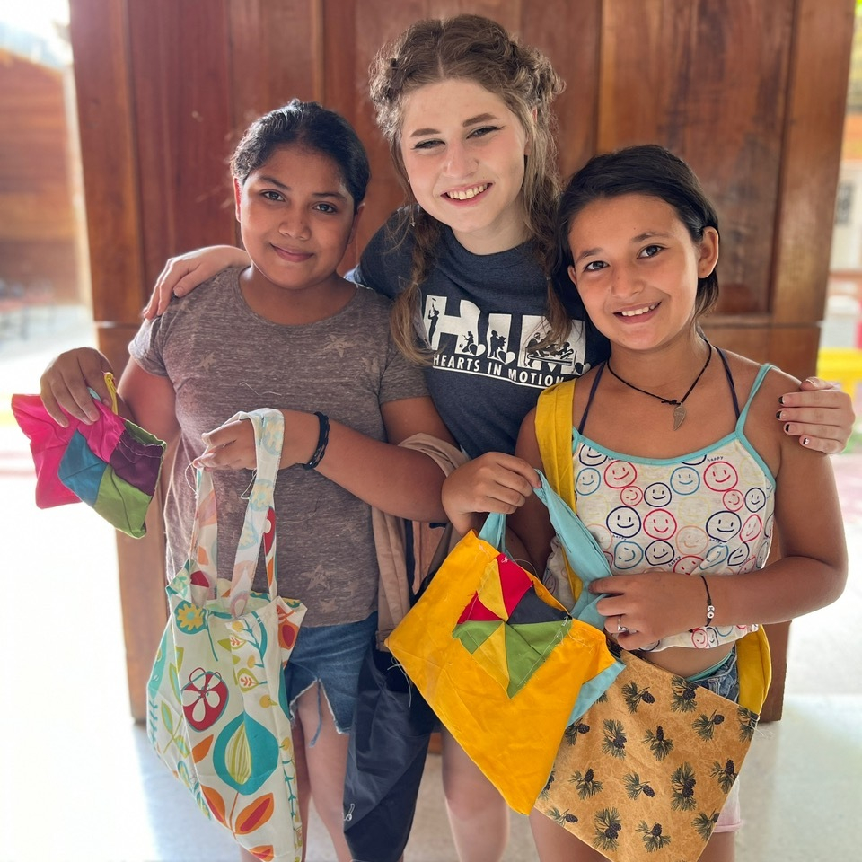 Three young ladies and two of them holding their tote bags.