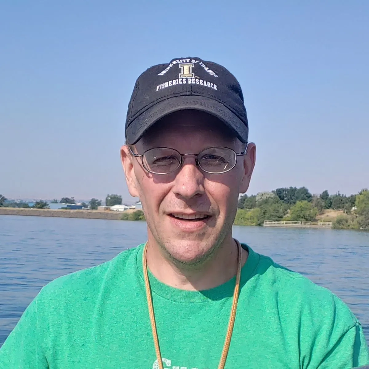 A man smiling with a University of Idaho hat on while being on a lake.