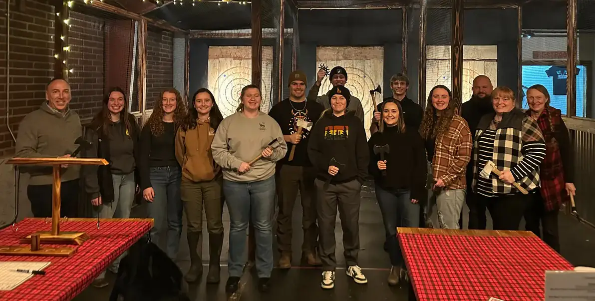 A line of students stands in in front of axe-throwing targets.