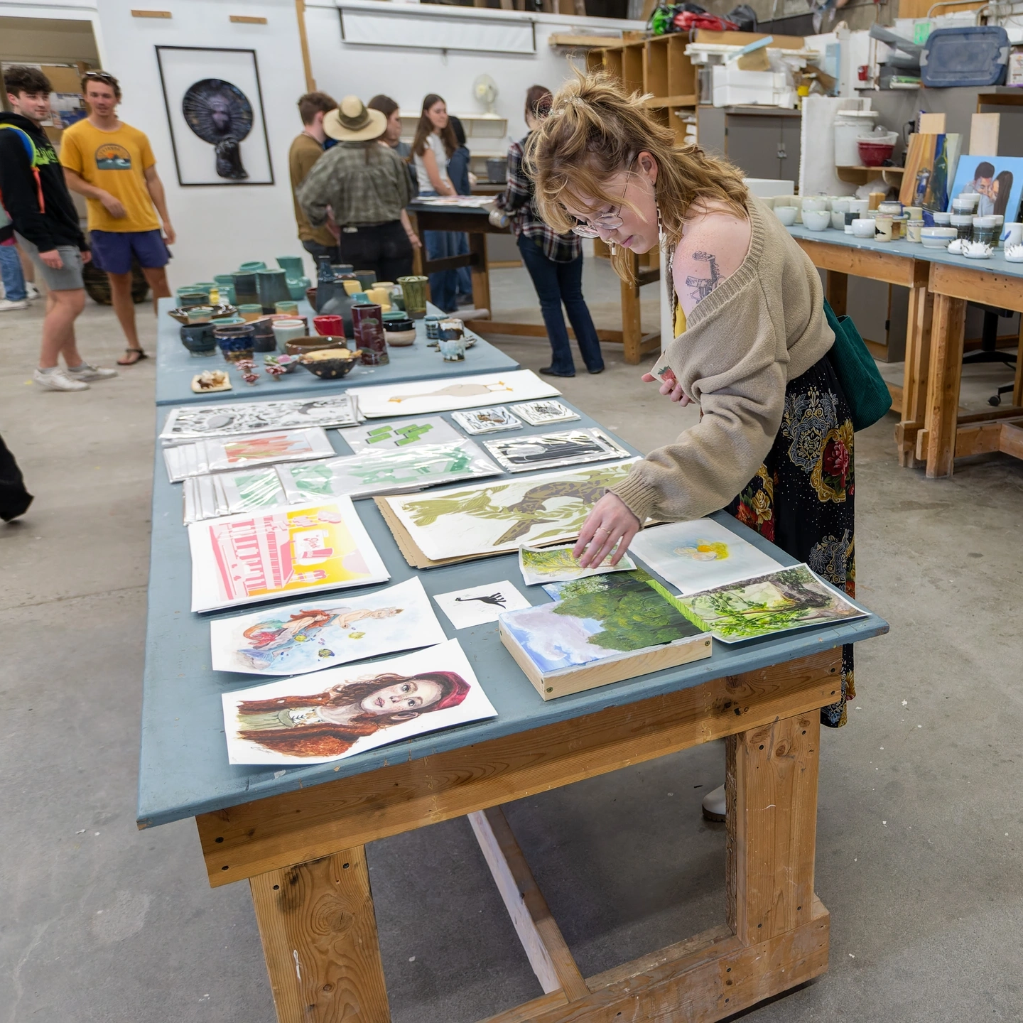 A student reaching for a painting that is sitting on a table with a bunch of others