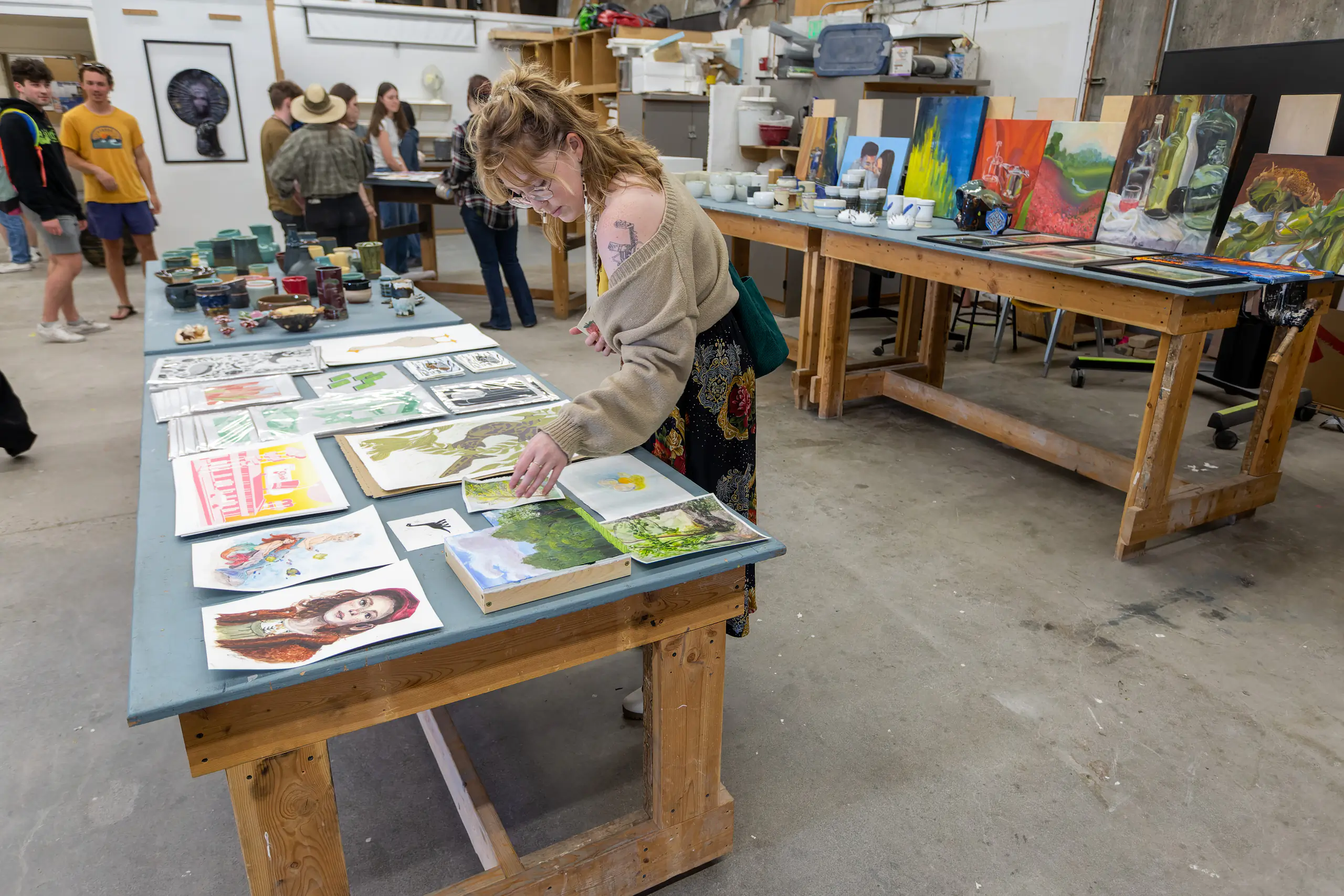 A student reaching for a painting that is sitting on a table with a bunch of others