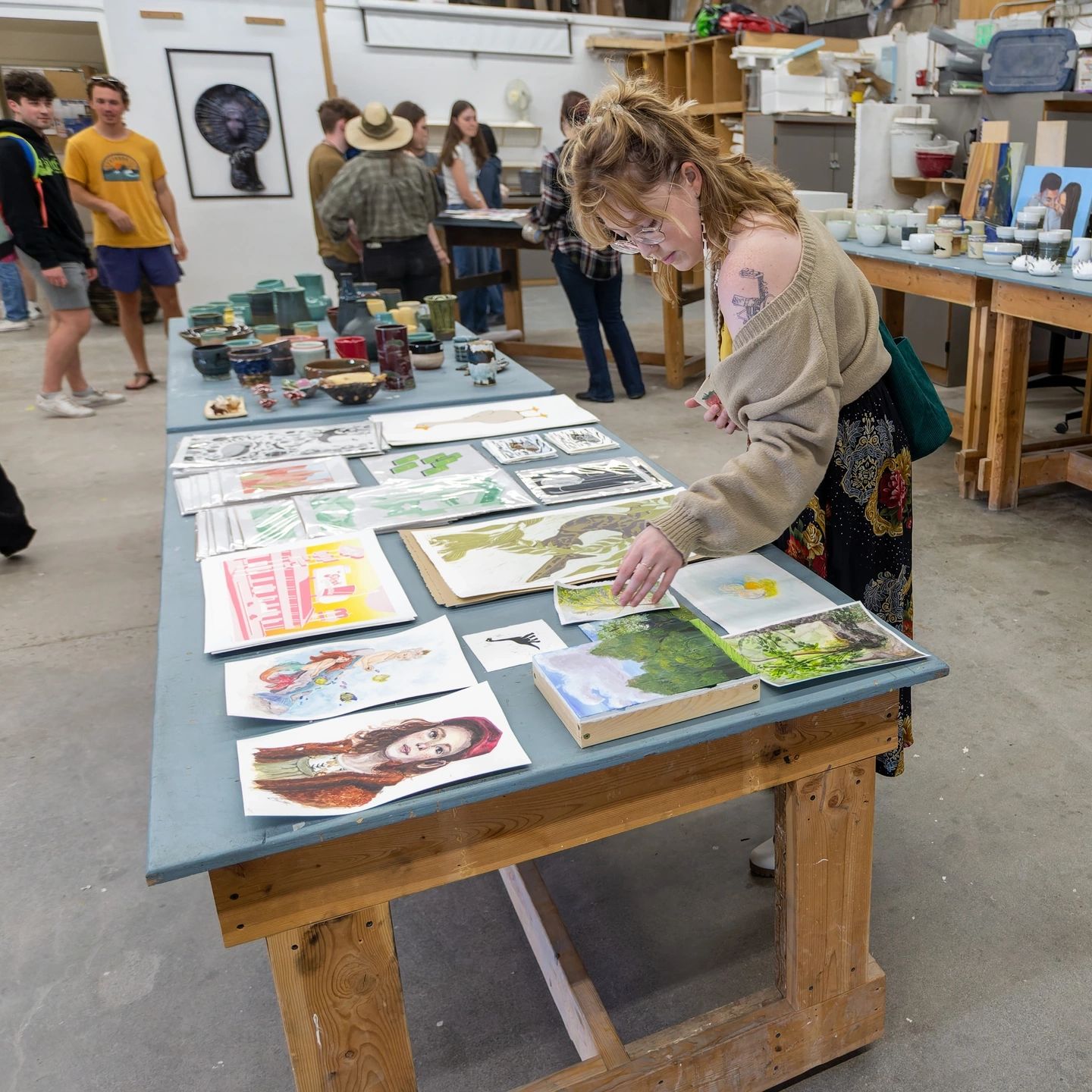 A student reaching for a painting that is sitting on a table with a bunch of others