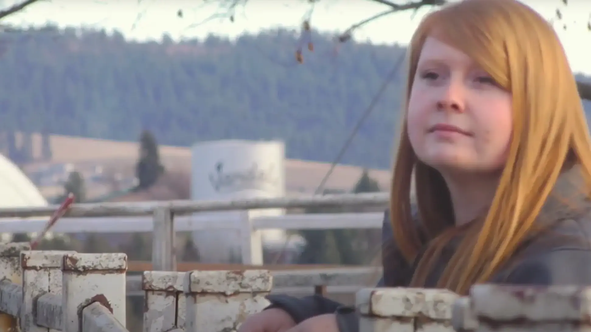 A woman leaning against a corral