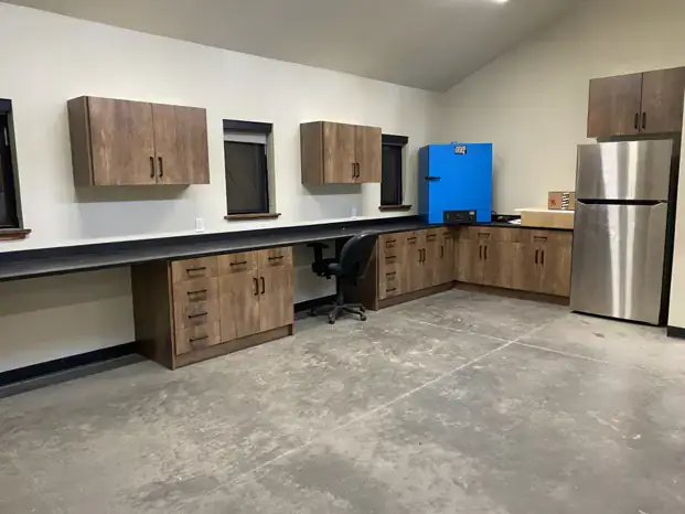 A workspace with wooden cabinets, countertop, windows, blue refrigerator, stainless steel fridge, and gray floor.