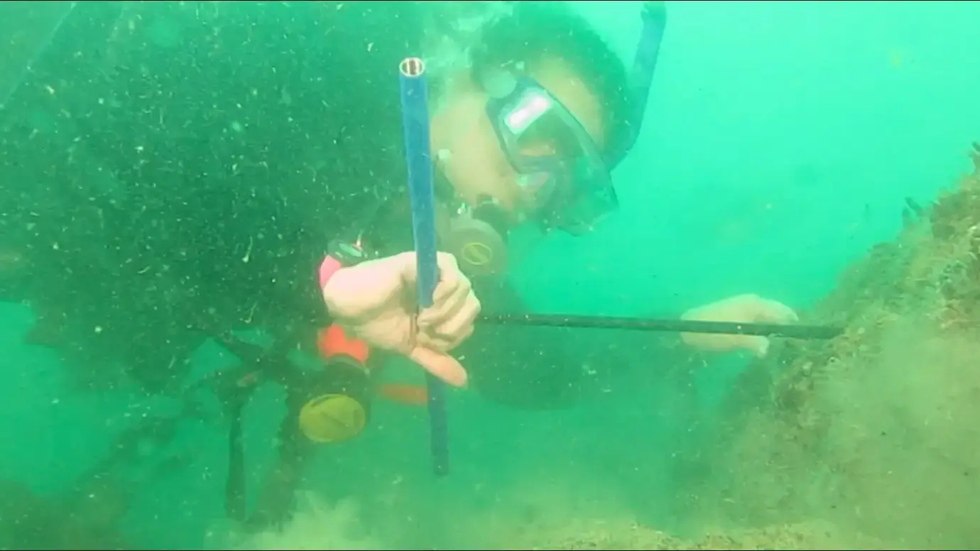 A person in scuba gear at the bottom of a ocean with a tool in their hand