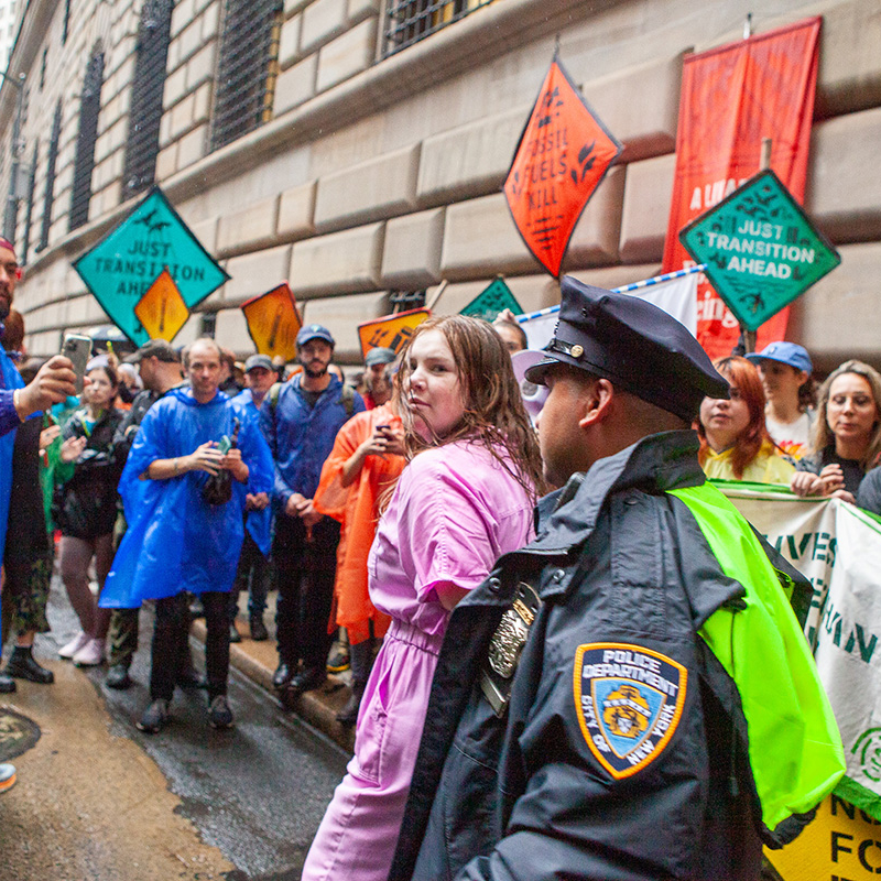 Woman in pink with police officer behind her surrounded by group of people.