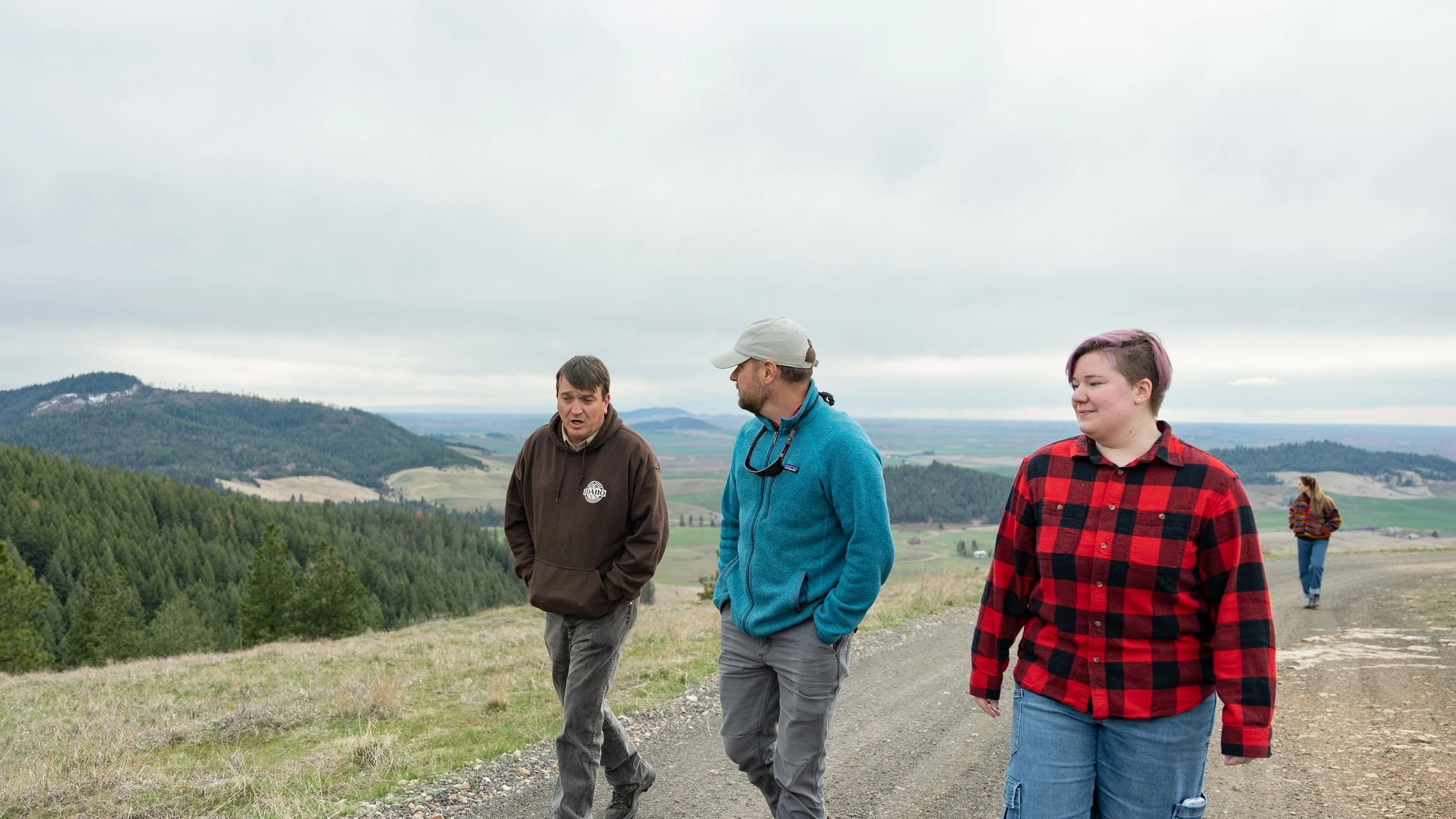 Four people walking on a dirt road above a view of the Palouse.
