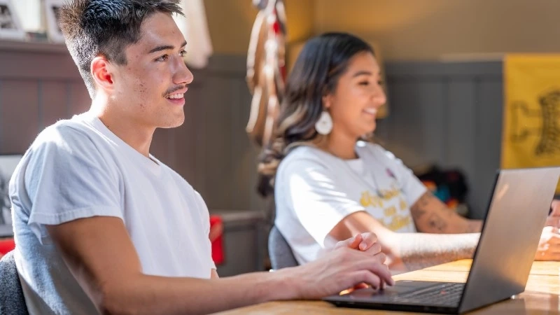 Two students on laptops smiling
