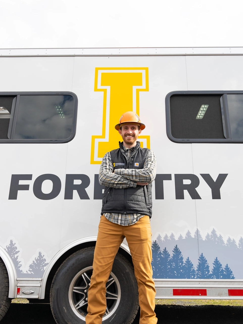 Man in a gold hardhat standing in front U of I-branded trailer.