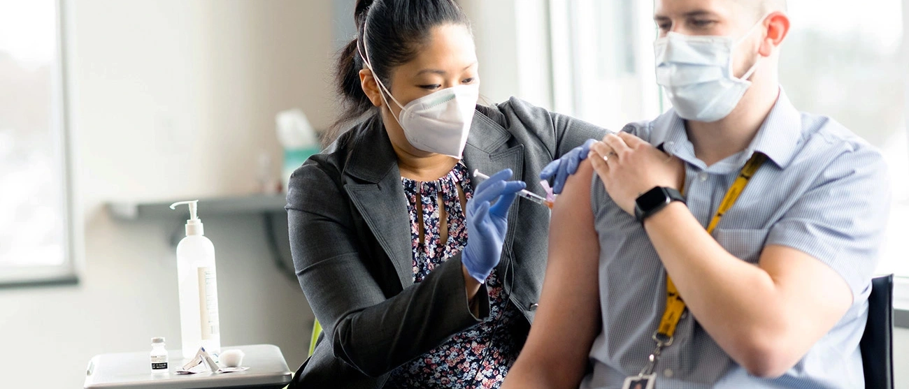 Guy getting a vaccine in his arm by a medical professional