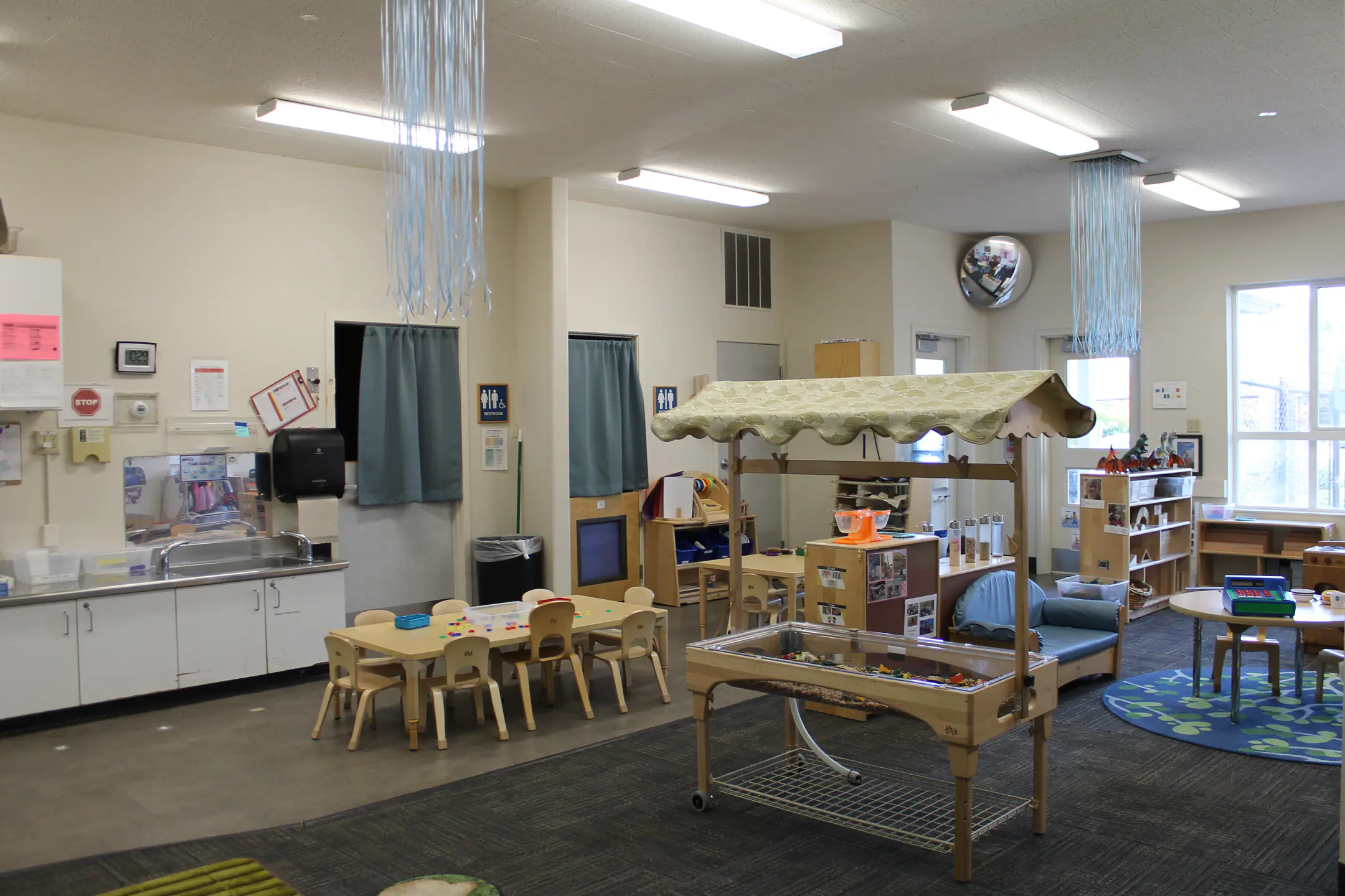 A large classroom with kitchenette, sensory table, group tables, and play area.