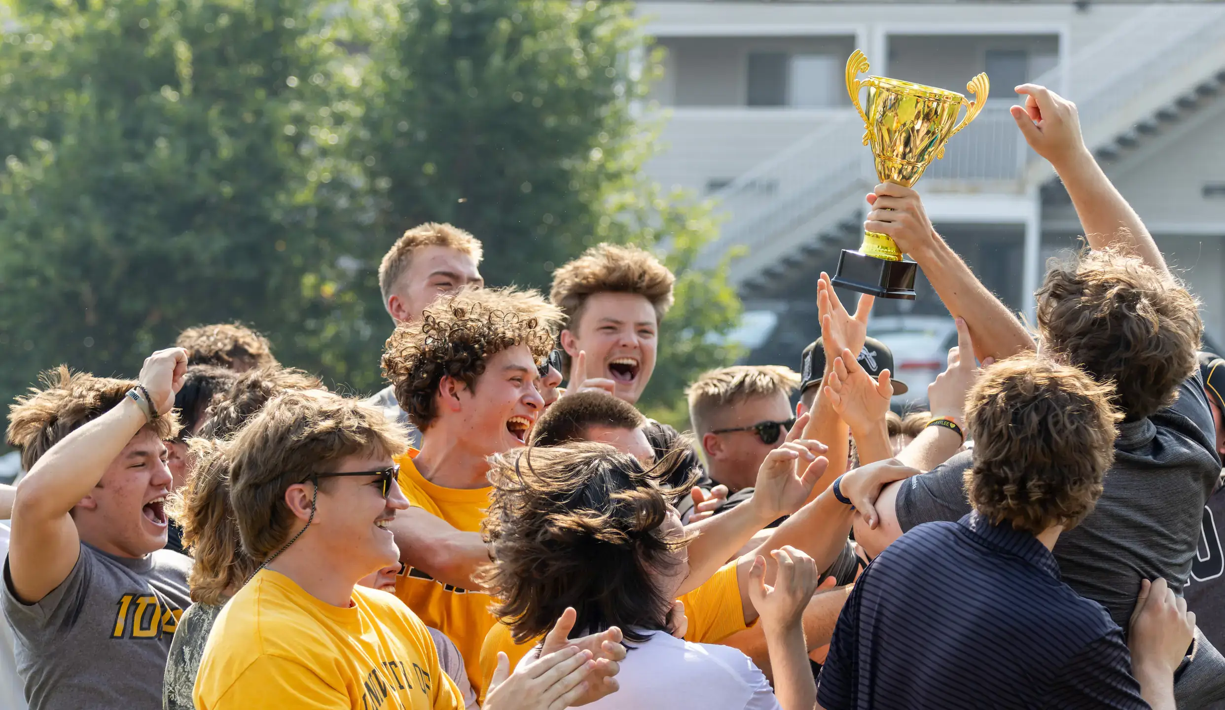 Students celebrating, with one student holding a trophy.