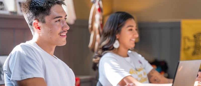 Two students on laptops smiling