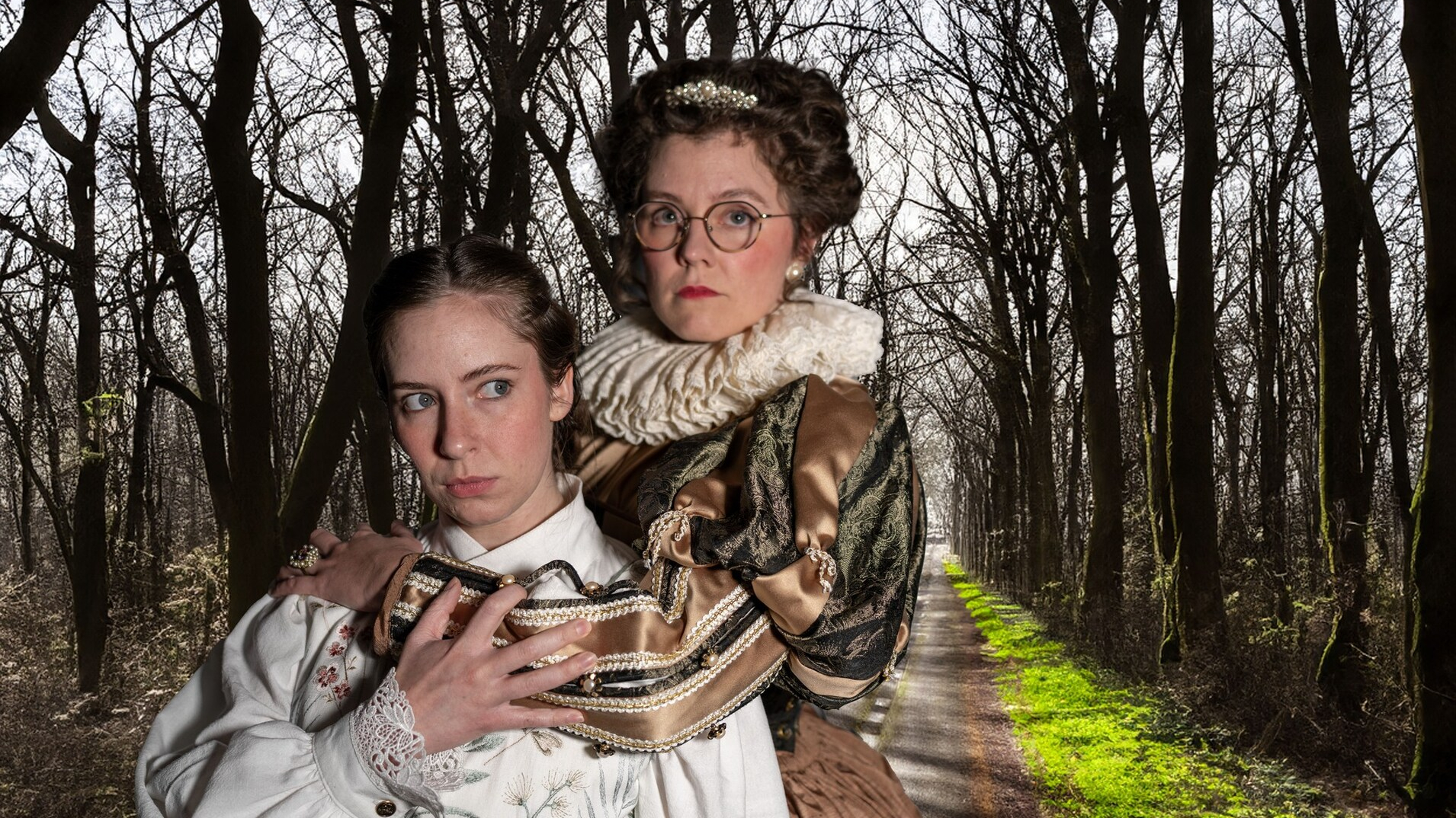 Two actors dressed in Elizabethan clothing embrace in front of wooded backdrop