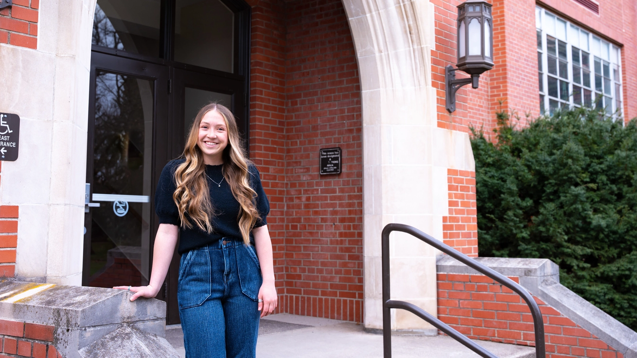 A woman poses next to a brick building on the University of Idaho campus.