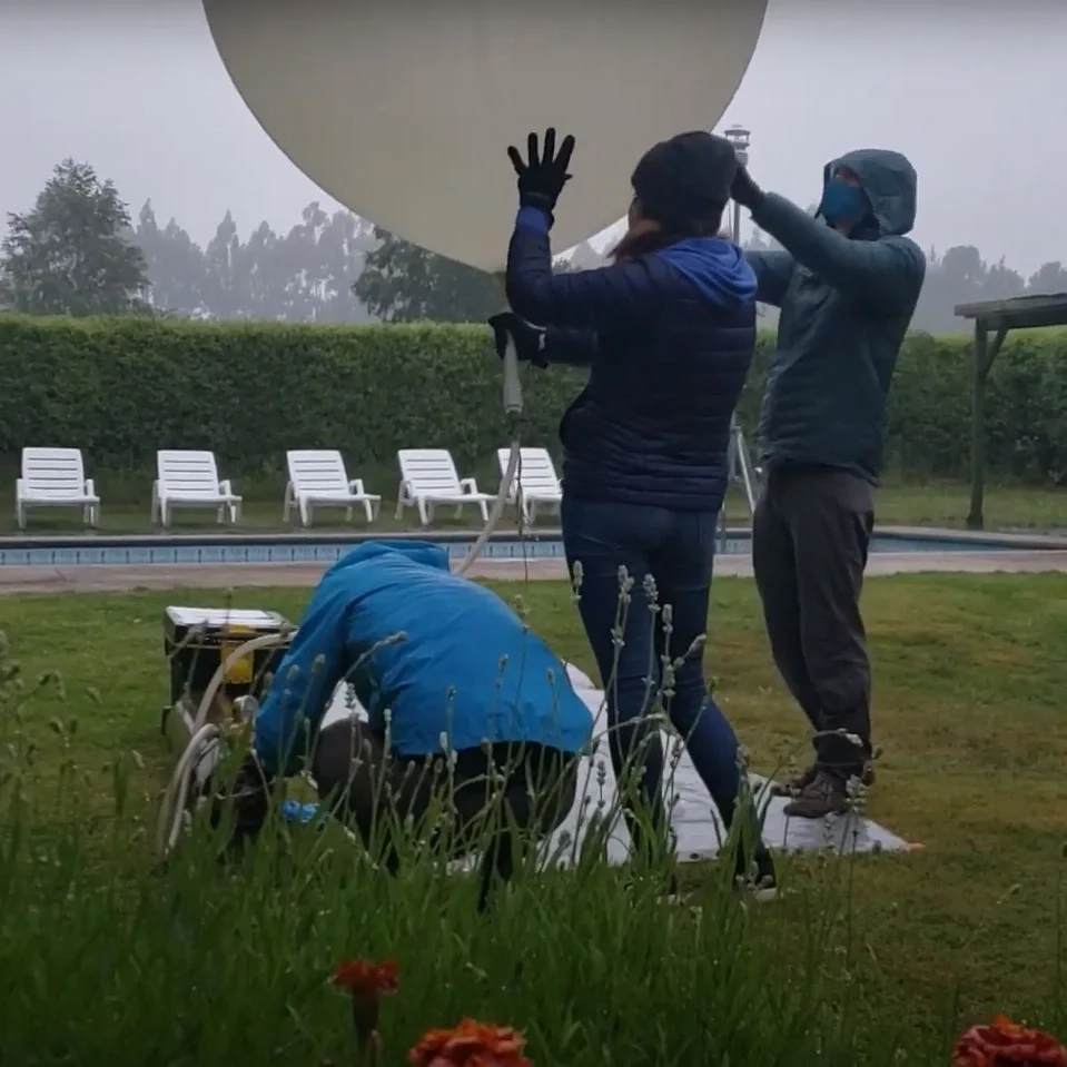Three people fill a white weather balloon in the rain. 