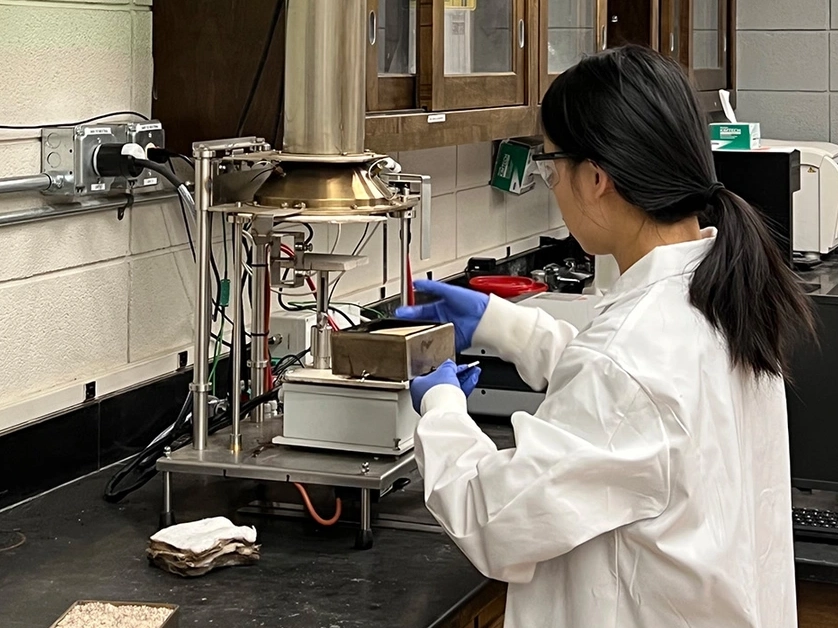 A woman in a white lab coat works under a chemical hood.