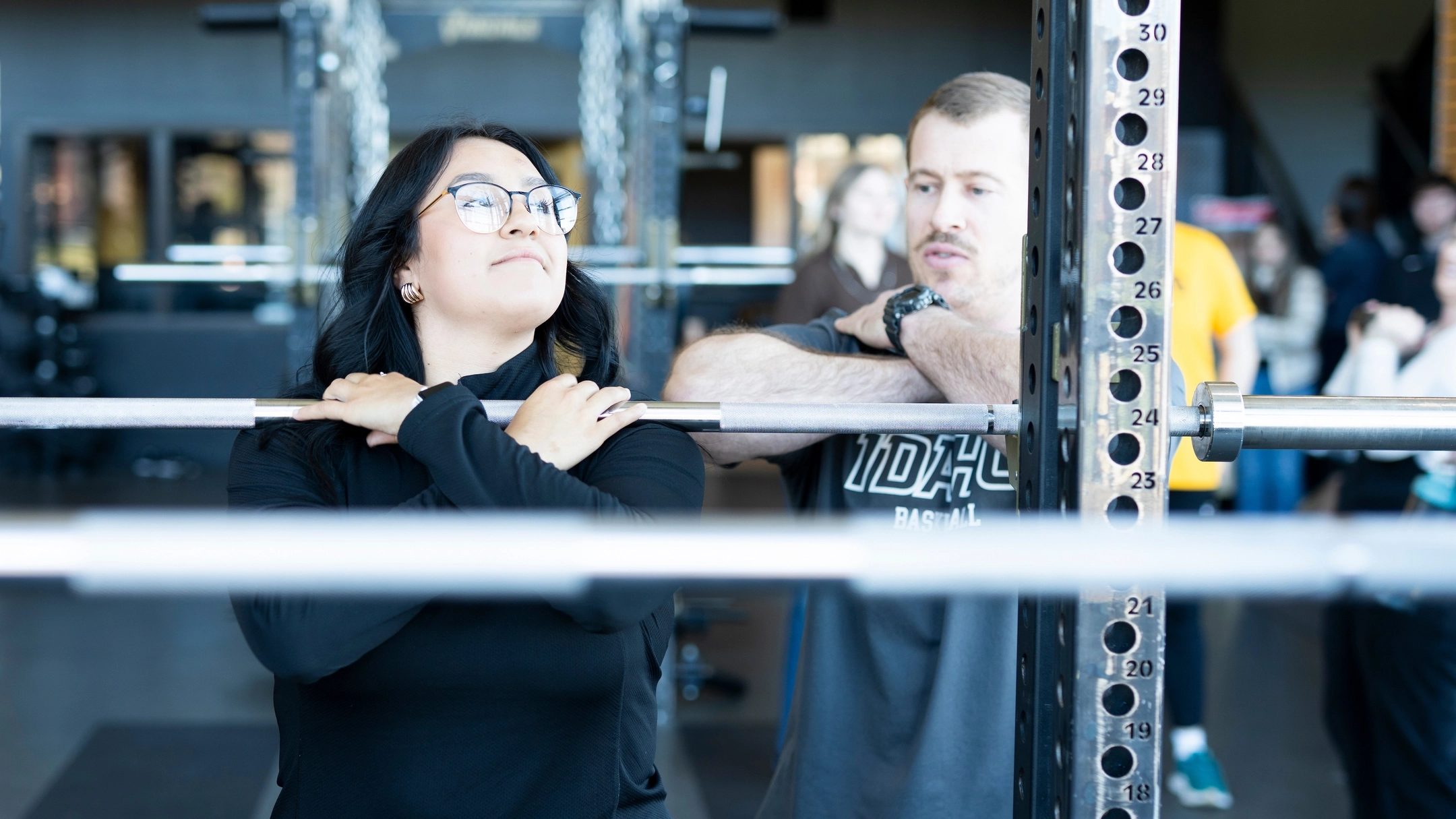 U of I athletic trainer helping a student lift weights  correctly in a weight room. 