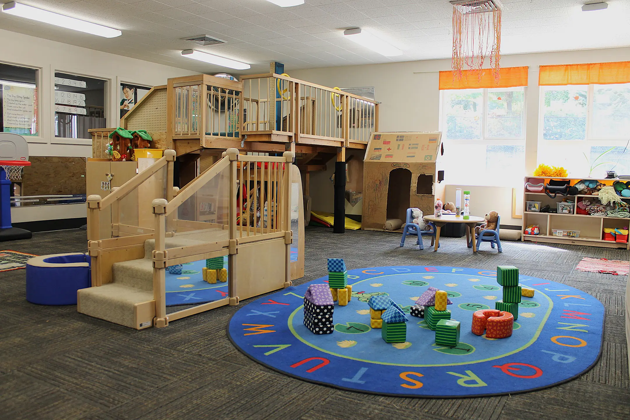 A play room with large, wooden jungle gym, play rugs, and building blocks.