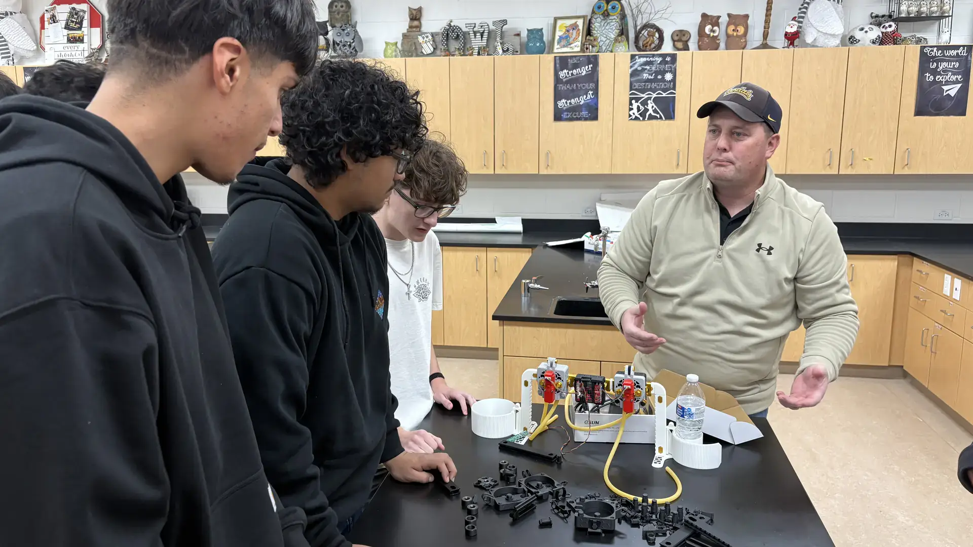 Three students stand along a table covered in plastic parts and electronic components as a University of Idaho Extension educator watches.